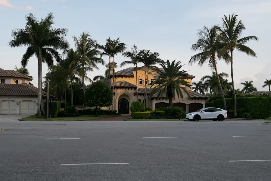 A tile-roofed house among tall palms across a wide street in Boca Raton