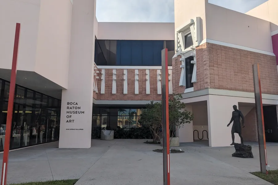 The entrance courtyard of the Boca Raton Museum of Art, with its name on a white wall and a bronze figure on a plinth